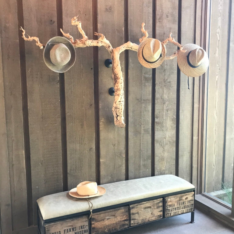 Grapevine mounted on wall being used as hat rack. 